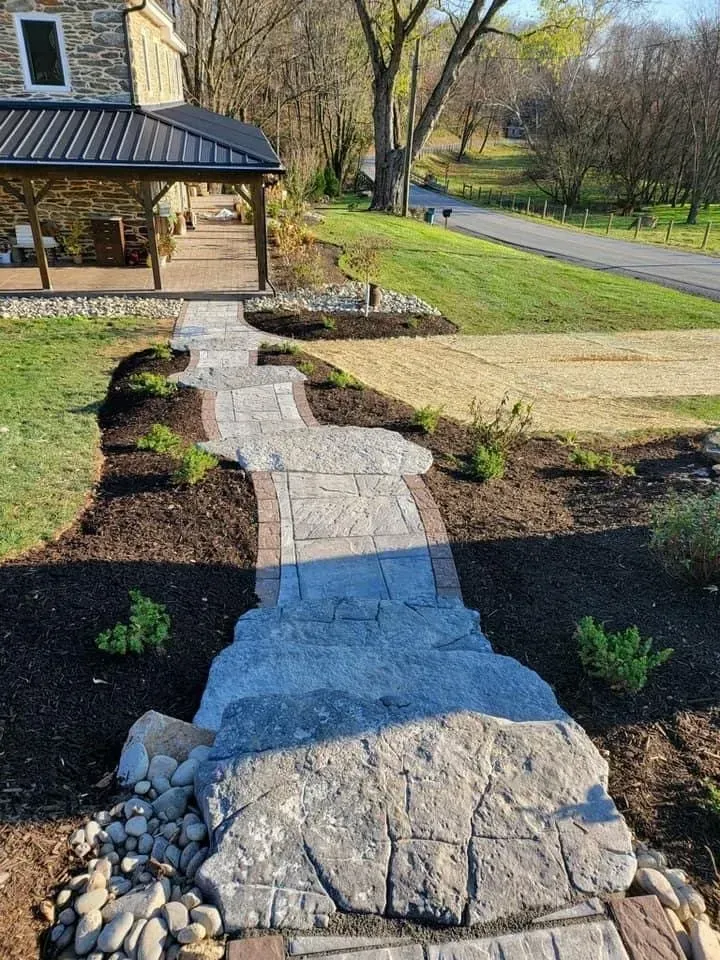 Stone walkway leading to a house with a porch, landscaping on either side.