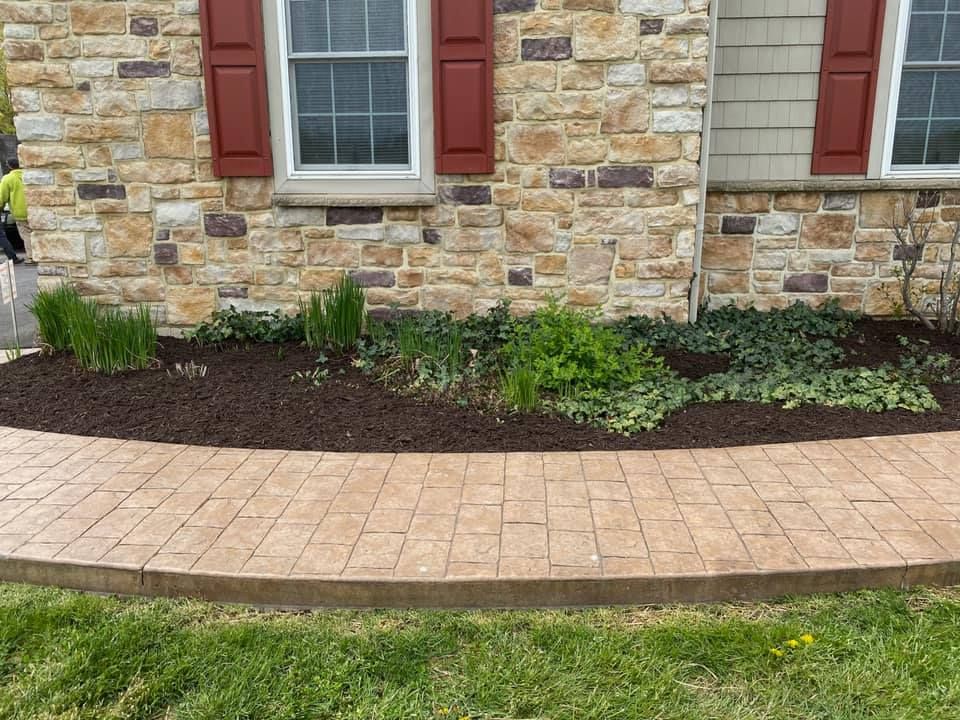 Stone building with red shutters, a brick walkway, and a landscaped bed of mulch and greenery.