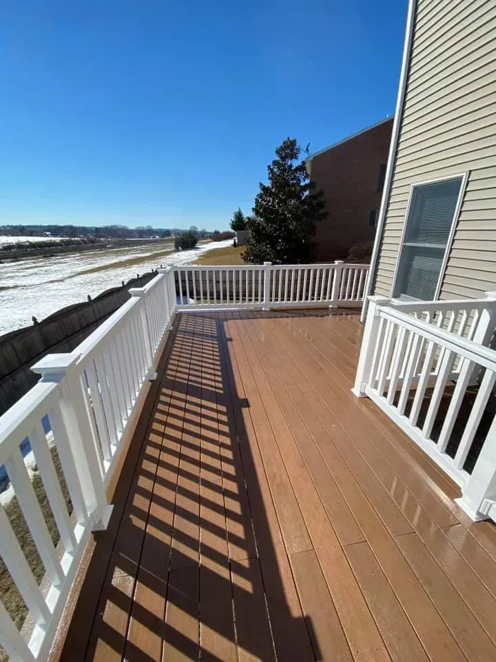Wooden deck with white railings, against a blue sky, overlooking a snowy landscape.