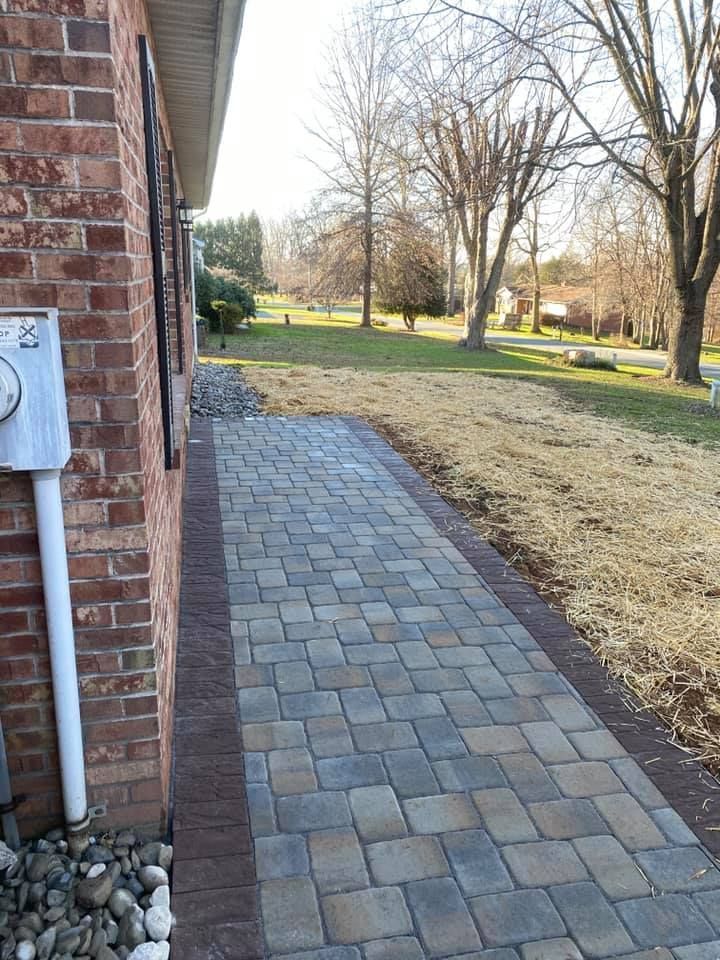 Brick home exterior with a paved walkway bordered by darker paving stones and adjacent grass.