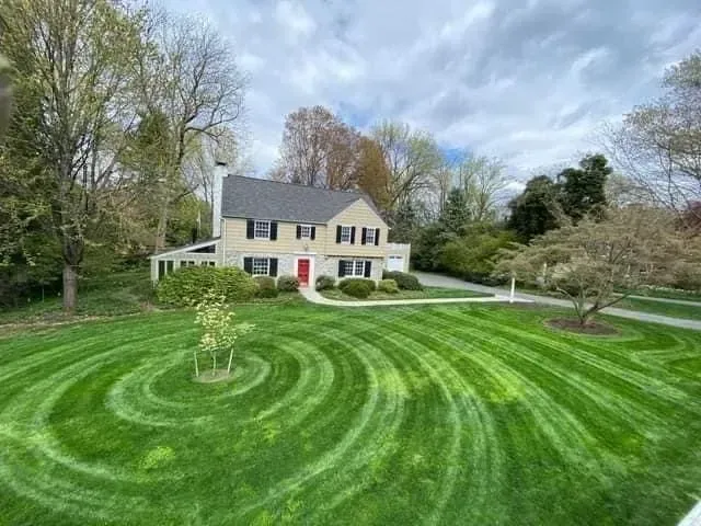 House with green lawn mowed in concentric circles, against a cloudy sky.