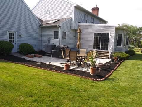 Backyard patio with outdoor furniture, edged with mulch, adjacent to a house with a sunroom and lawn.