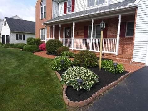 A house with a well-manicured lawn, garden beds, and a porch.