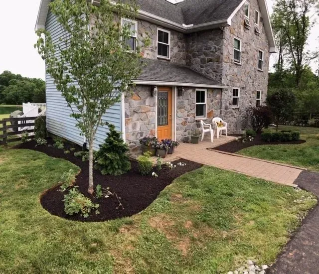 Stone house with blue siding, orange door, and a brick walkway. Landscaping with mulch and grass.