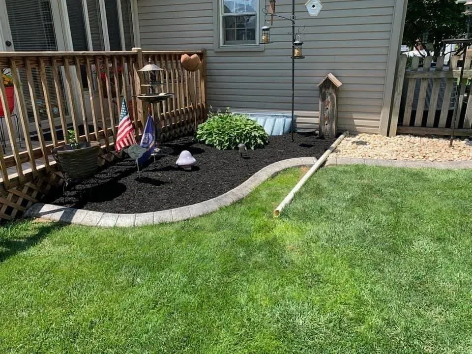 Lawn with a mulch bed, deck, and house. Flags and bird feeders are in the mulch.
