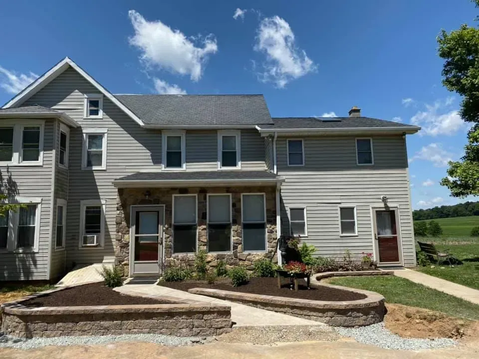 Two-story house with gray siding and stone facade, landscaping, and clear blue sky.