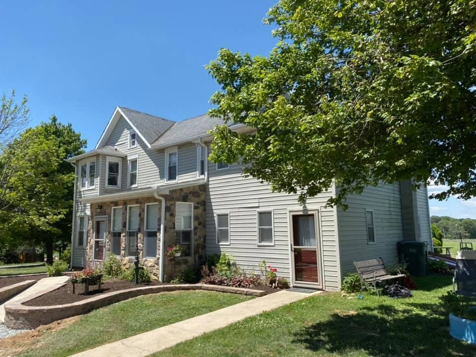 Two-story house with stone and siding facade, flanked by trees, under a blue sky.