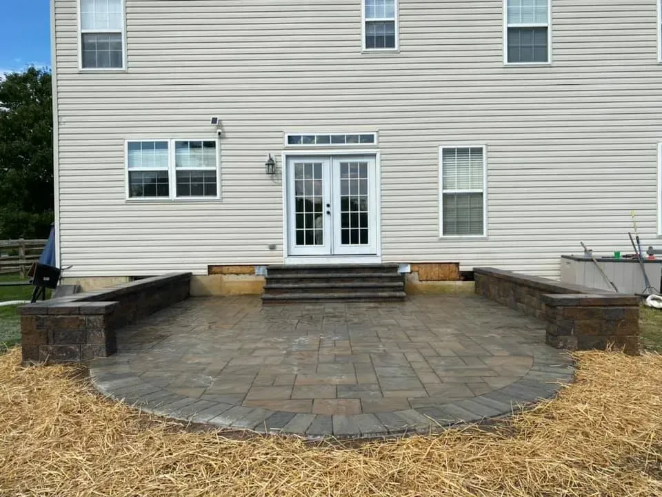Back patio with brick pavers, raised brick walls, steps to french doors, and a beige house.
