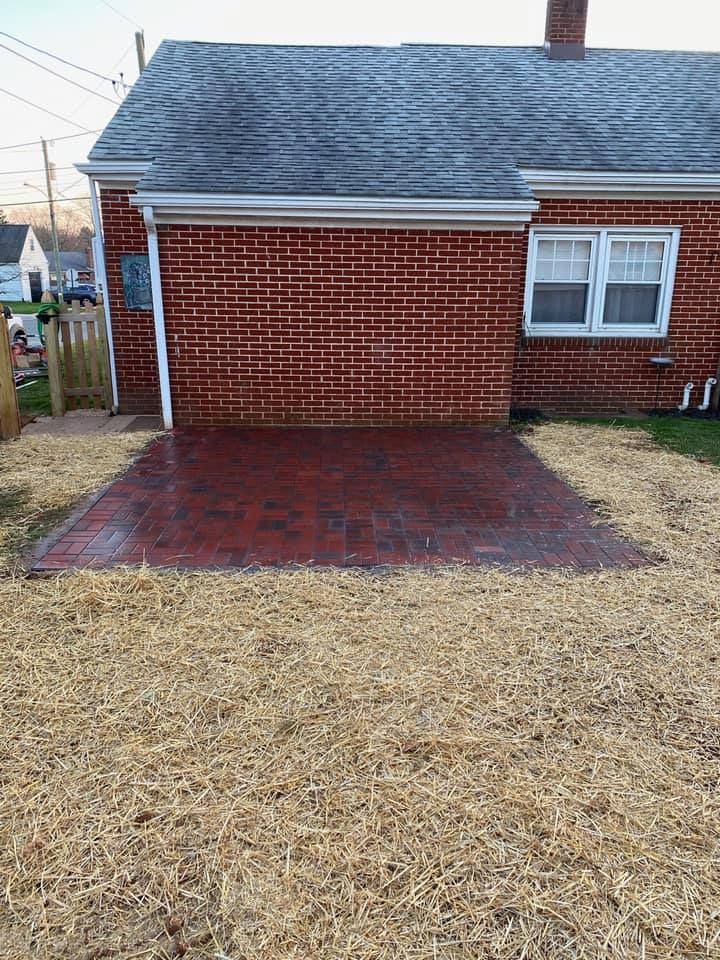 Red brick patio next to a red brick house with a brown, dead grass lawn.
