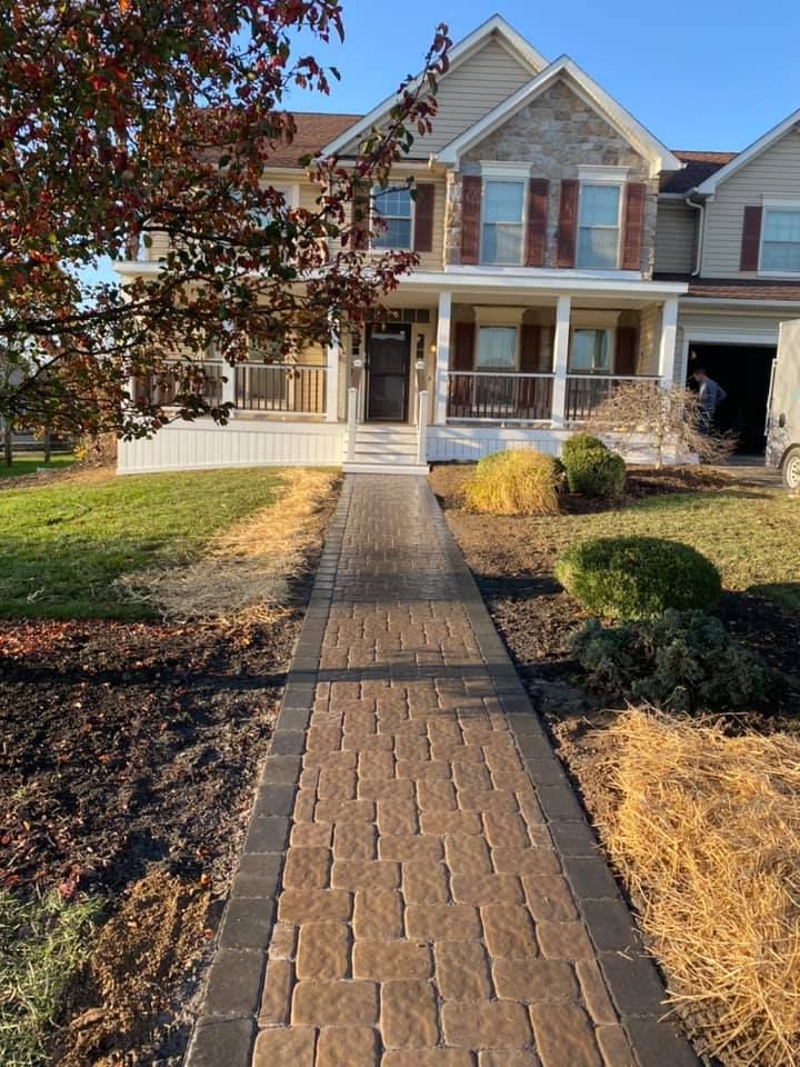 Brick walkway leading to a two-story house with a porch and landscaped yard.