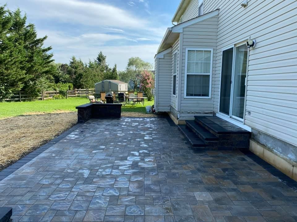 Backyard patio with pavers, low wall, and steps leading to a sliding door.