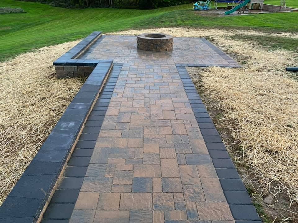 Brick patio with fire pit, bordered by dark brick and retaining walls, set in a grassy yard.