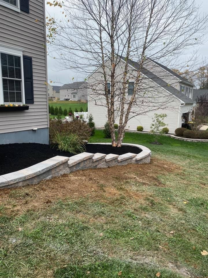A house with a raised stone garden bed around a tree and lawn.