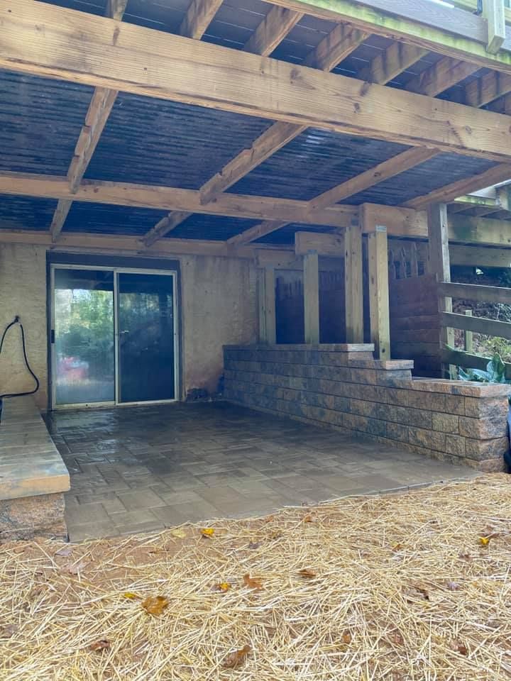 Stone patio under wooden deck with sliding glass door and retaining wall.