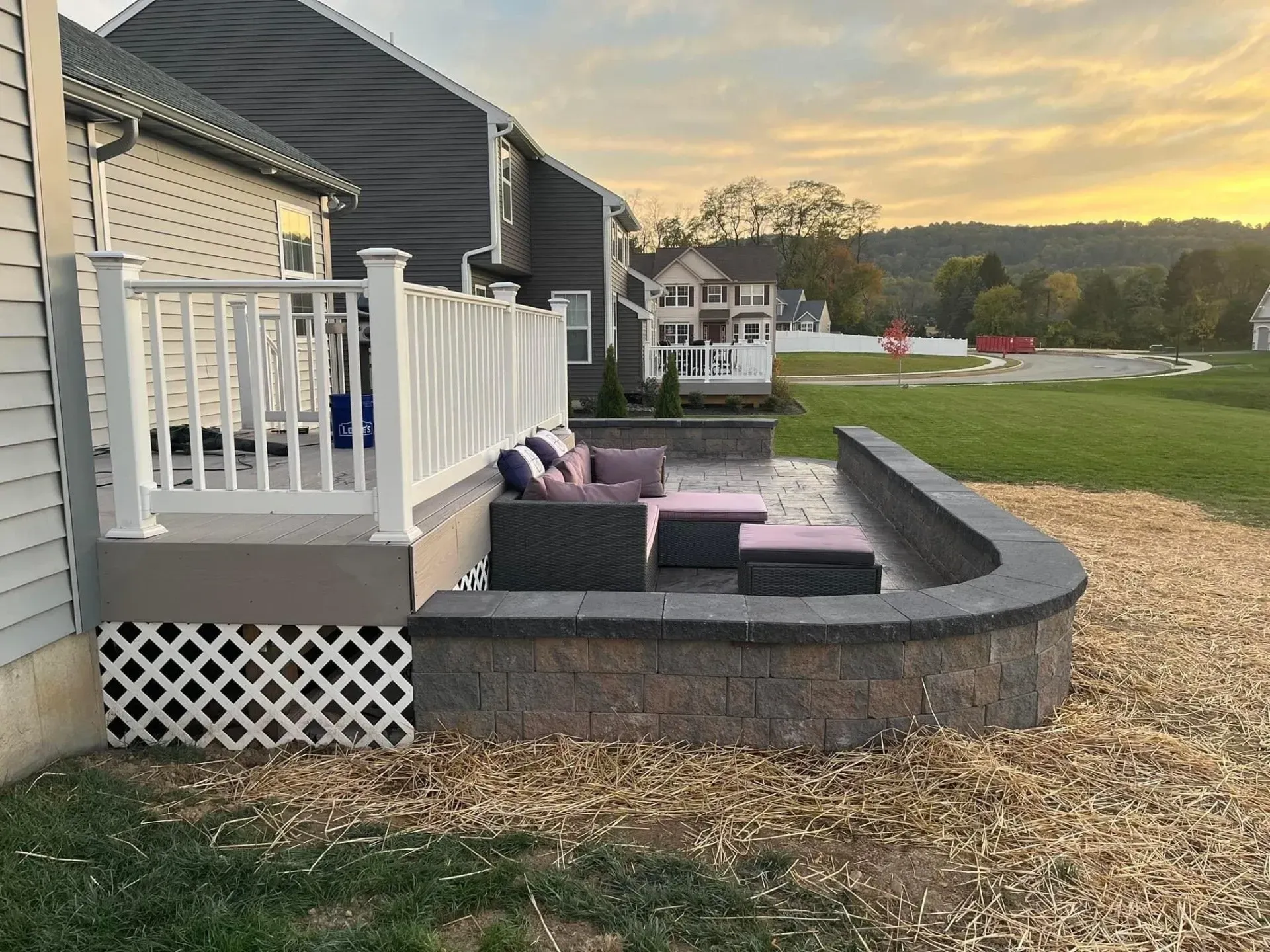 Backyard patio with seating, stone wall, deck with white railing, and grassy area.