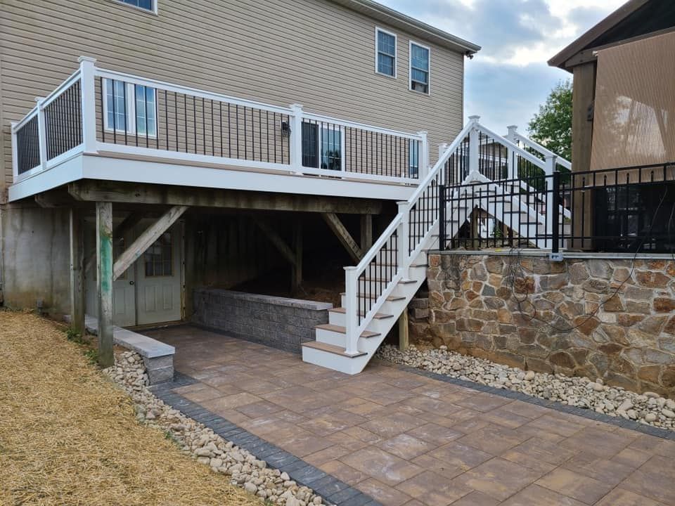 A deck with stairs, a paved pathway, and retaining walls next to a beige house.