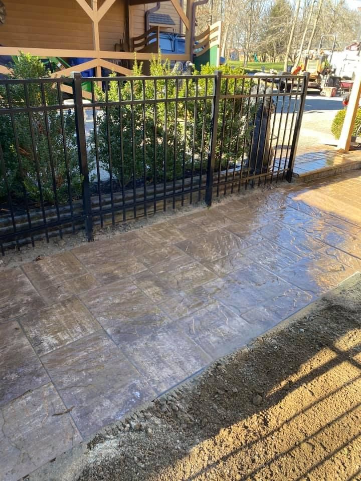Black metal fence next to a paved patio, with a green building and street visible.