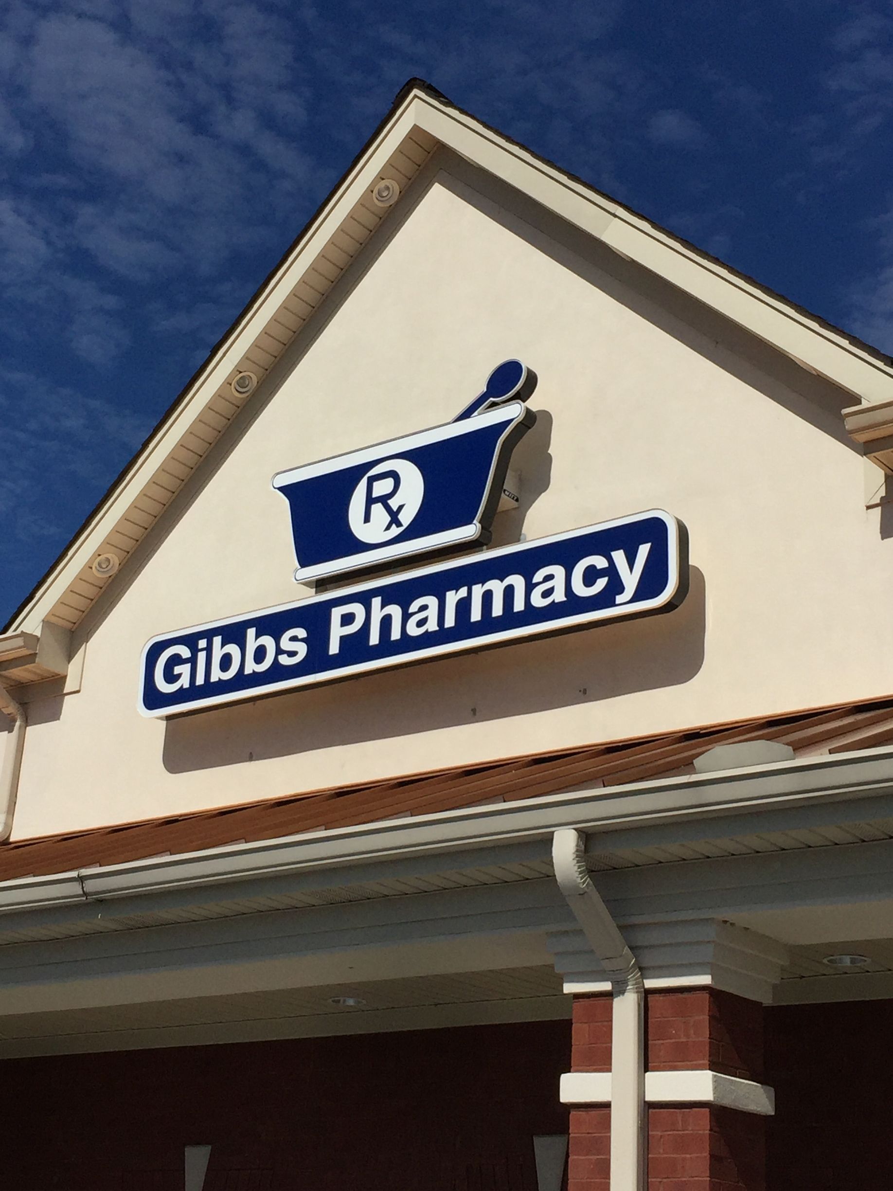 A white building with a blue sign that says gibbs pharmacy