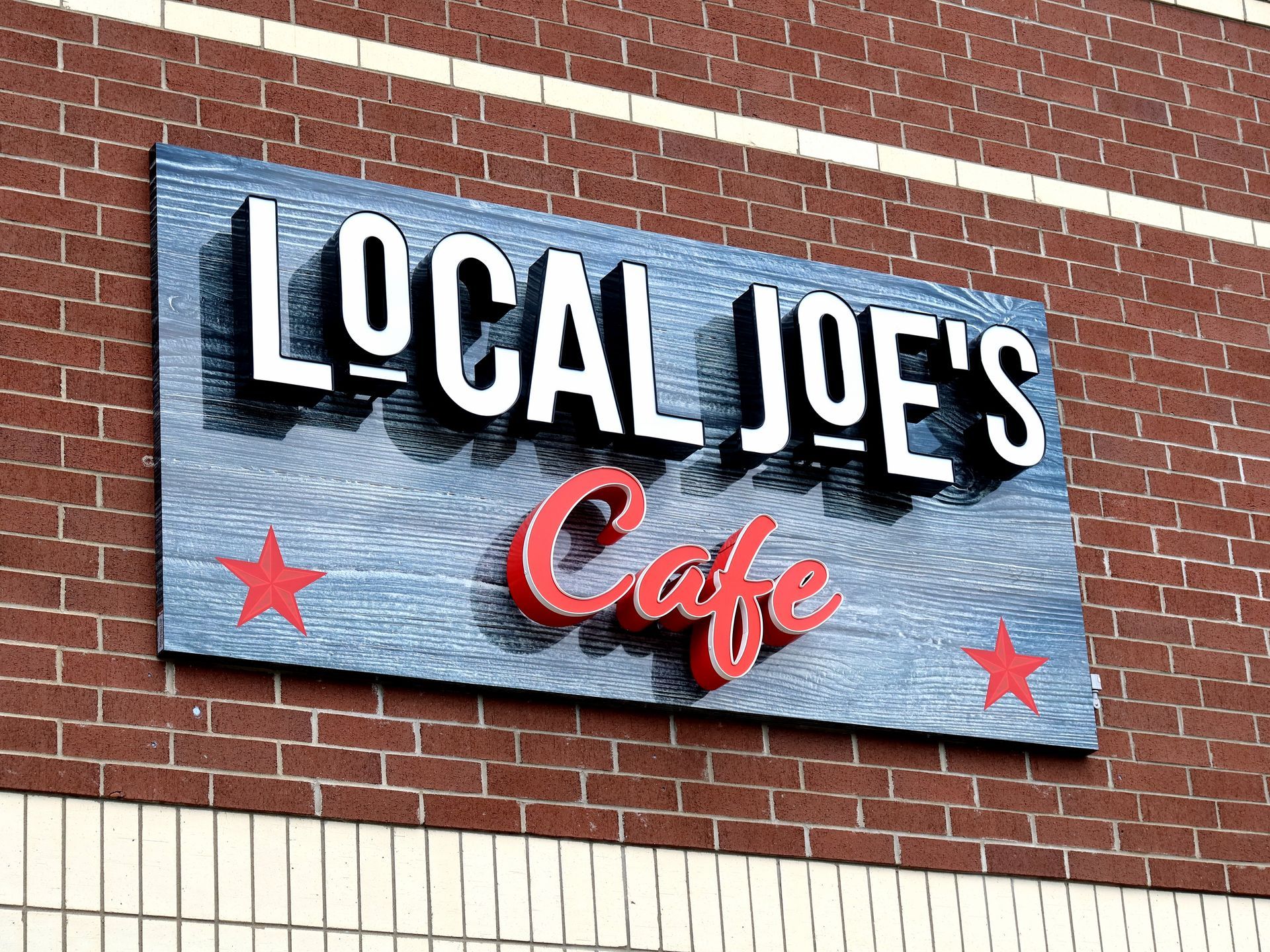 A sign for local joe 's cafe is on a brick wall