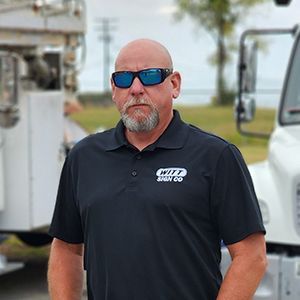 A man wearing sunglasses and a black shirt is standing in front of a truck.