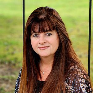 A woman with long brown hair is sitting on a swing in a field.