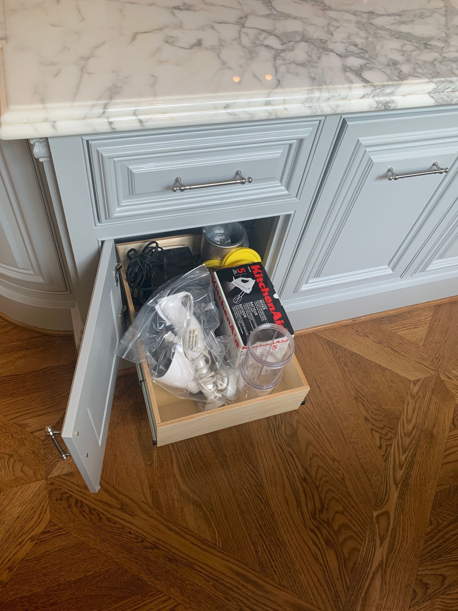 A light blue cabinet with a drawer open, revealing items inside, under a marble countertop.