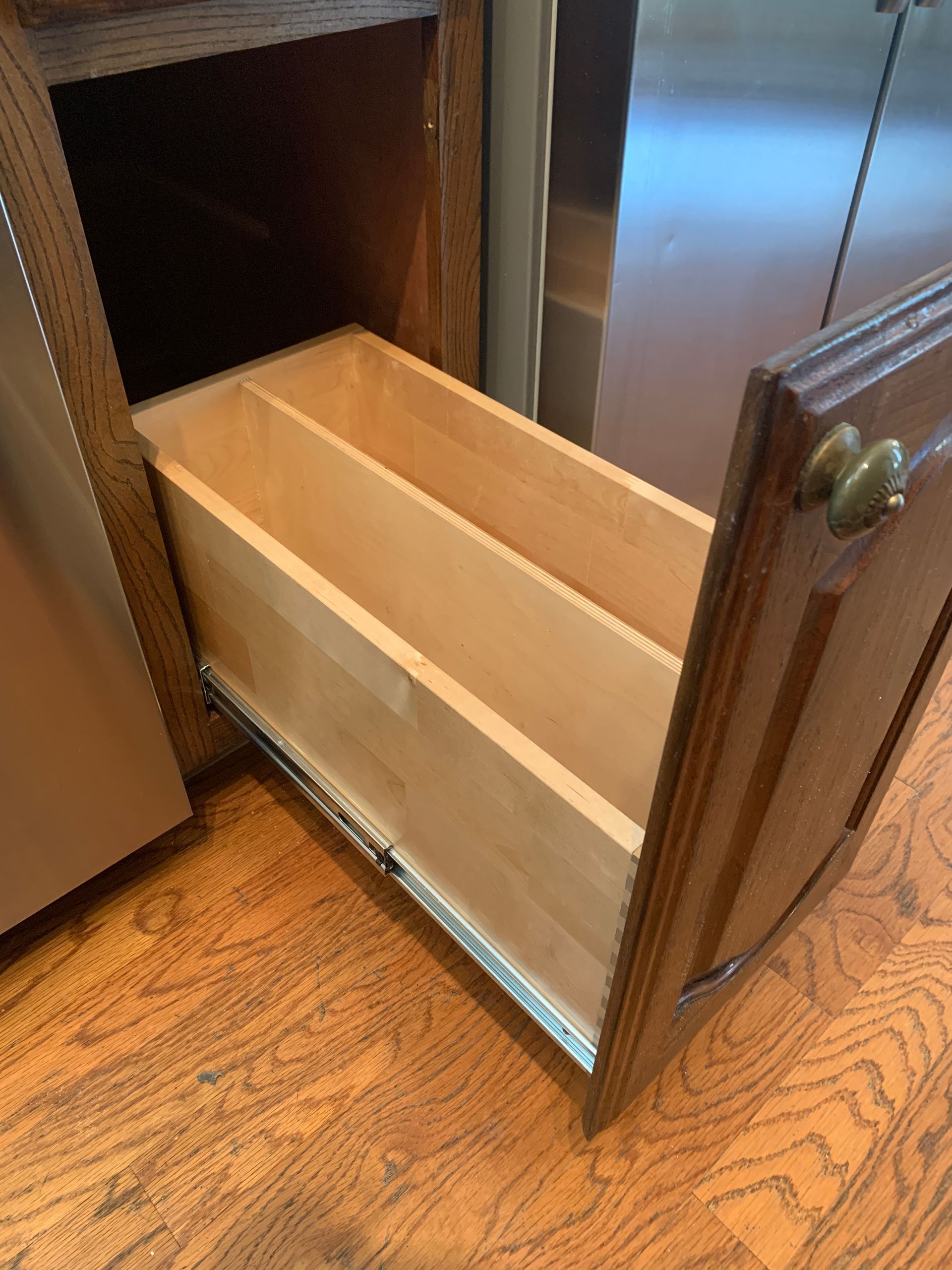 Open wooden kitchen drawer with two dividers, in a brown cabinet on a wood floor.