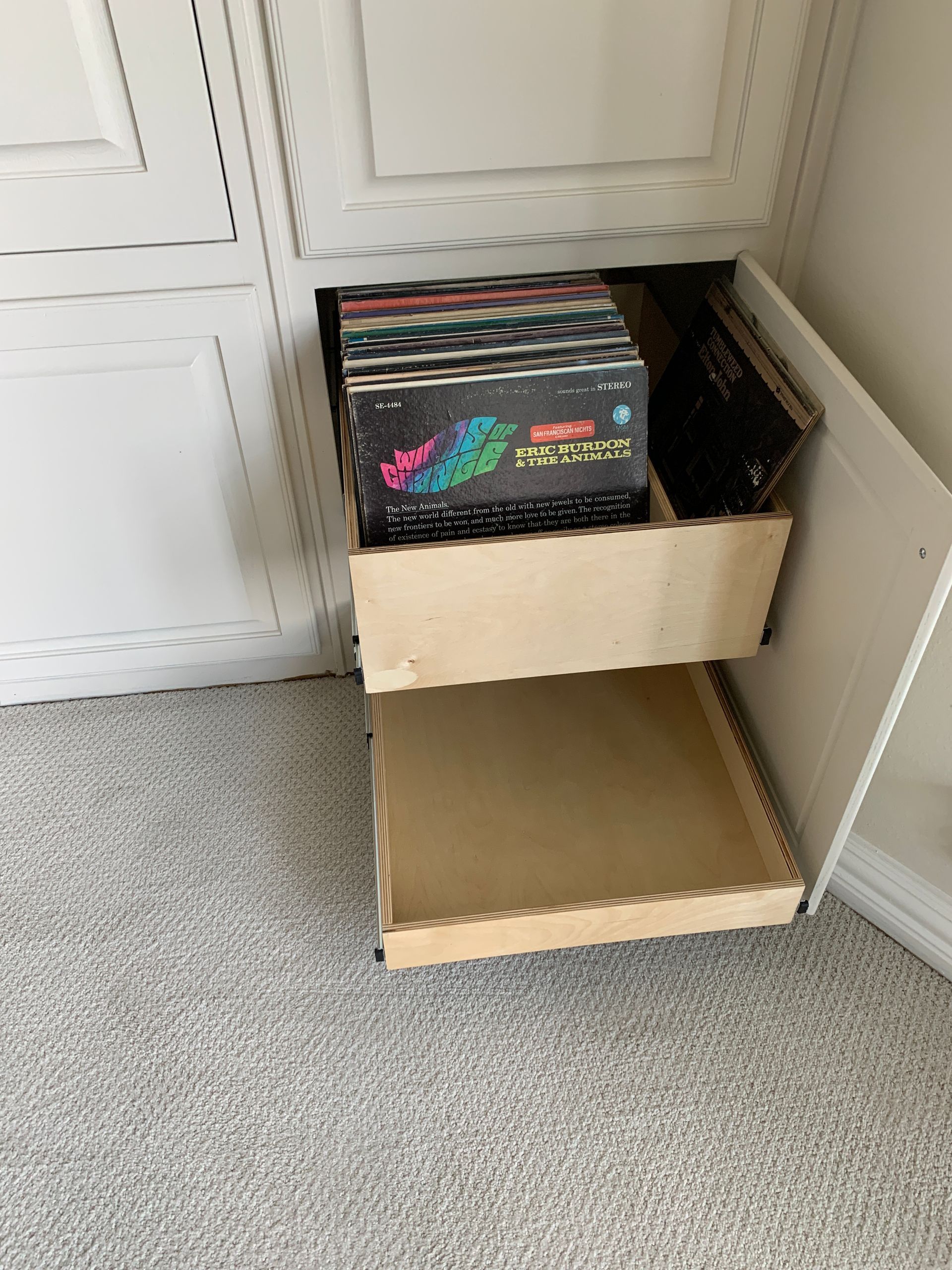 White cabinet with open drawer holding vinyl records, another empty drawer below.