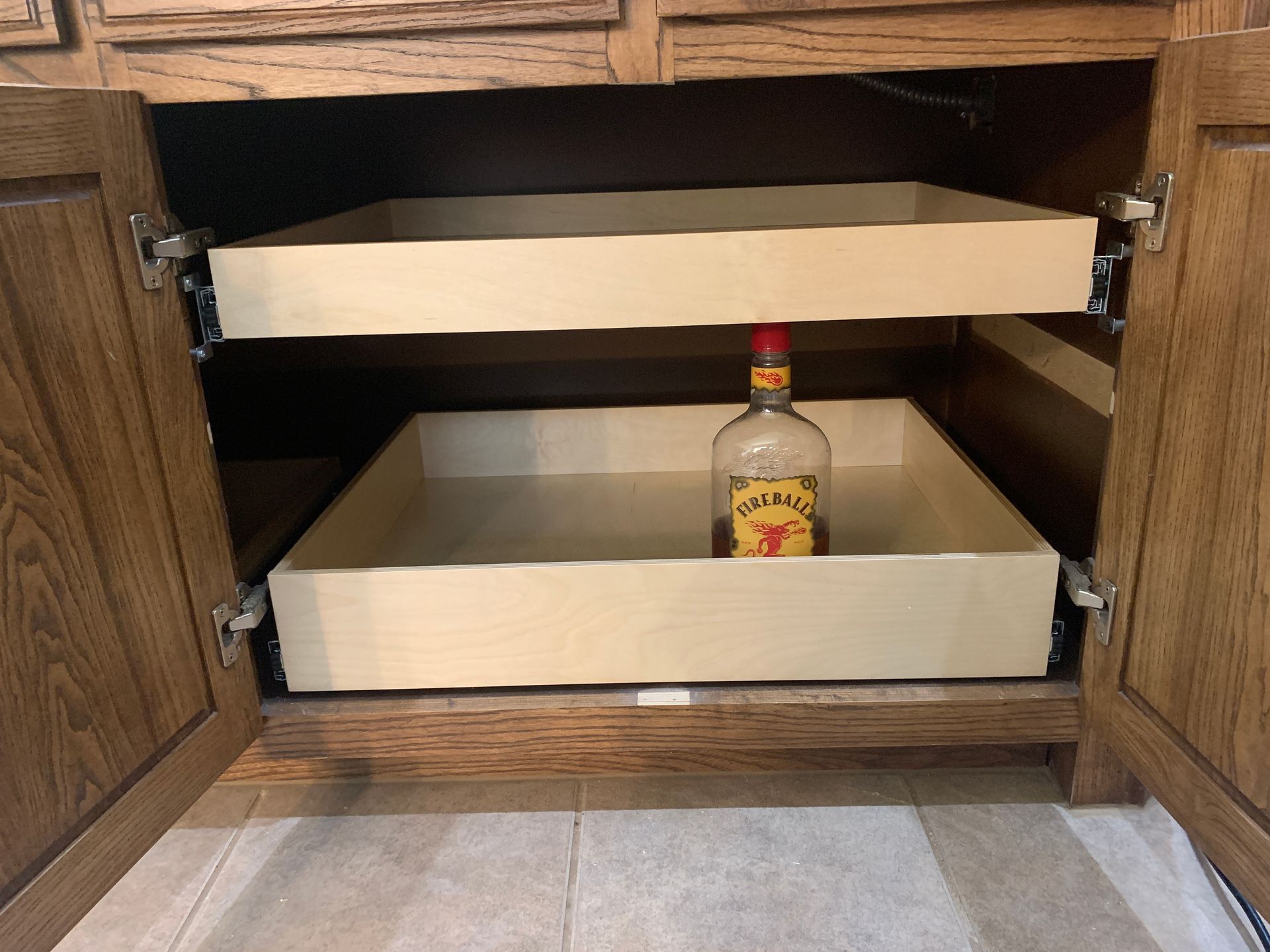 Inside cabinet with two pull-out shelves; a bottle of liquor sits on the bottom shelf.