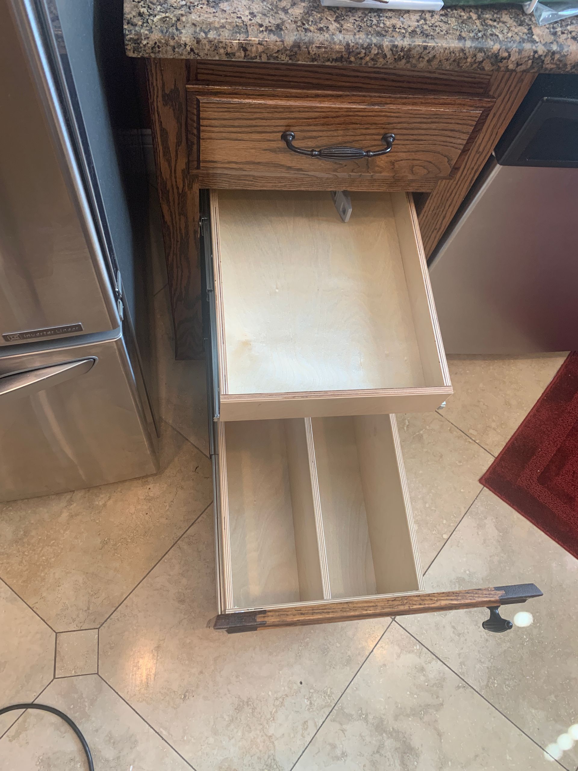 Open kitchen drawer with a silverware organizer, near a refrigerator and granite countertop.