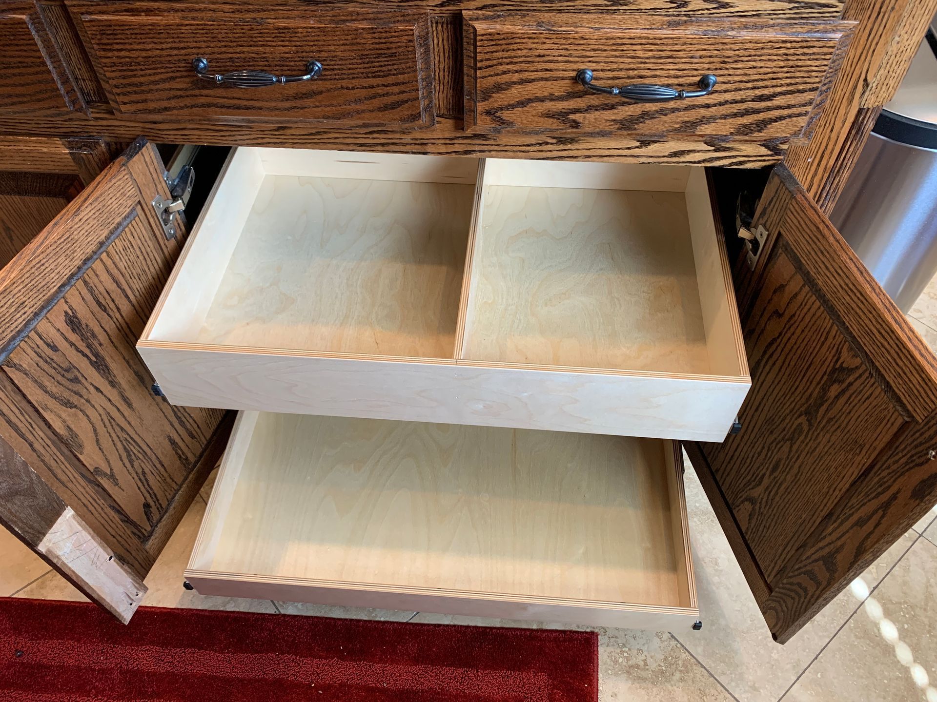 Open kitchen cabinet with two shallow drawers pulled out, light wood.