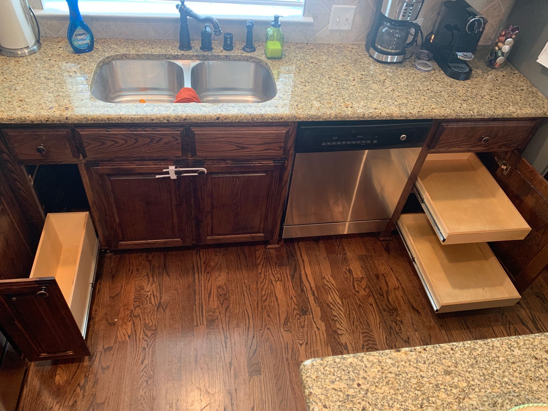 Kitchen cabinets: sink, dishwasher, pull-out drawers, open cabinet doors, hardwood floor, granite countertop.