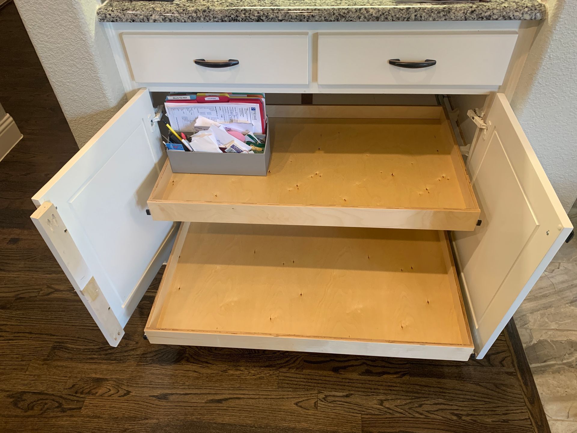 White kitchen cabinet with two pull-out shelves. A box with papers sits on the top shelf.