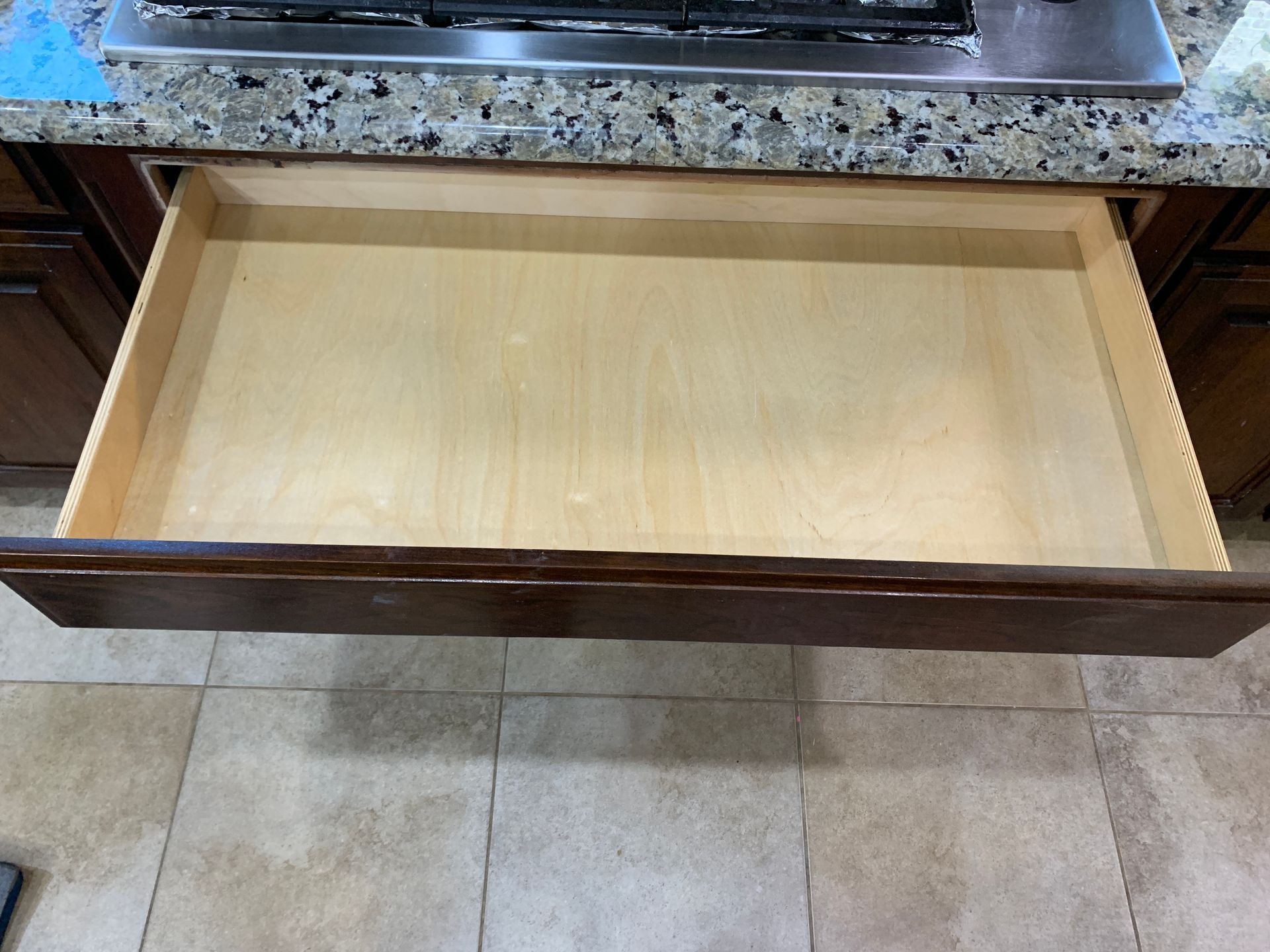 Open wooden kitchen drawer under a countertop with a granite surface.