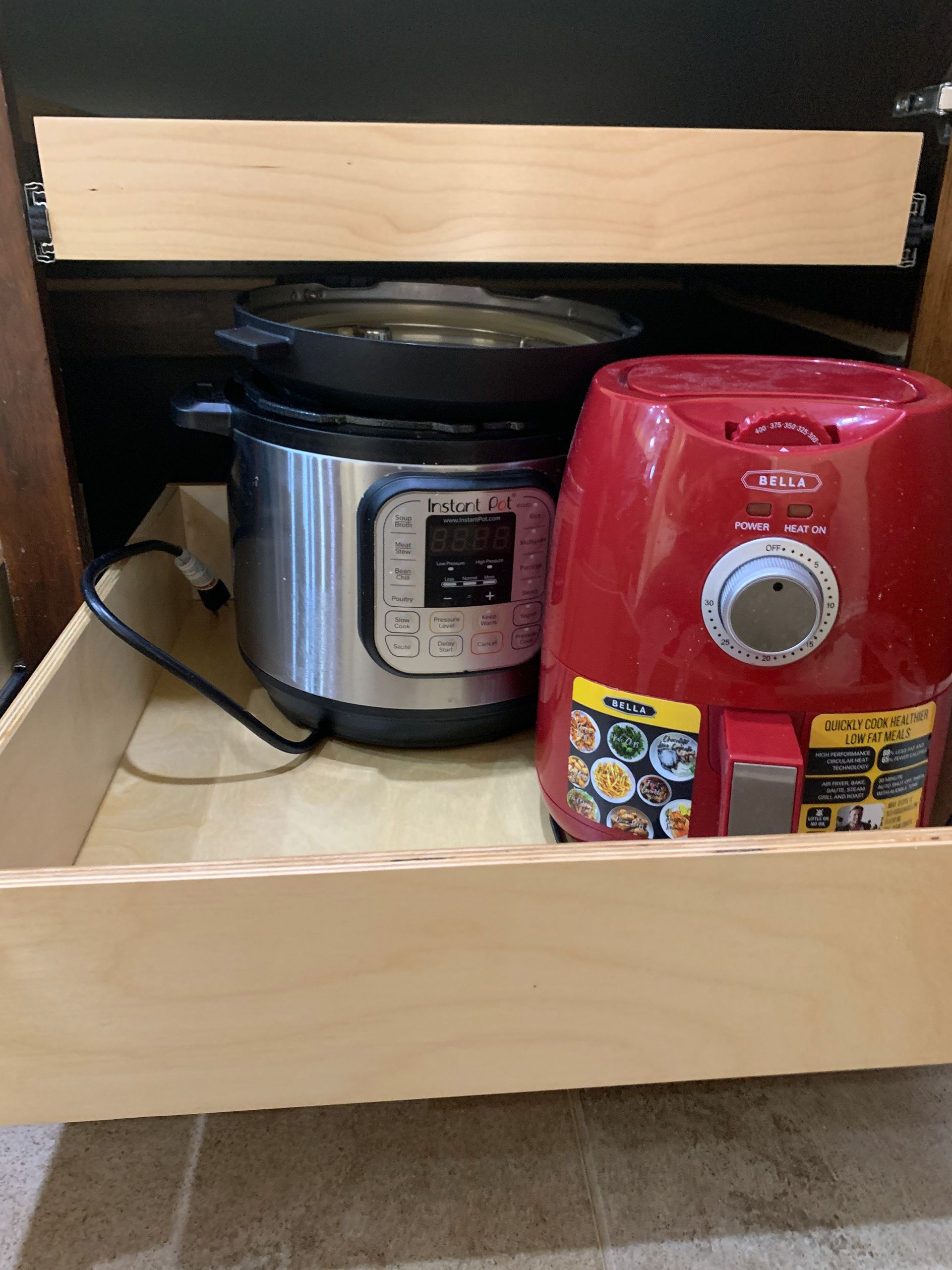 An open kitchen drawer holds a silver Instant Pot, a red air fryer, and a black cast iron skillet.