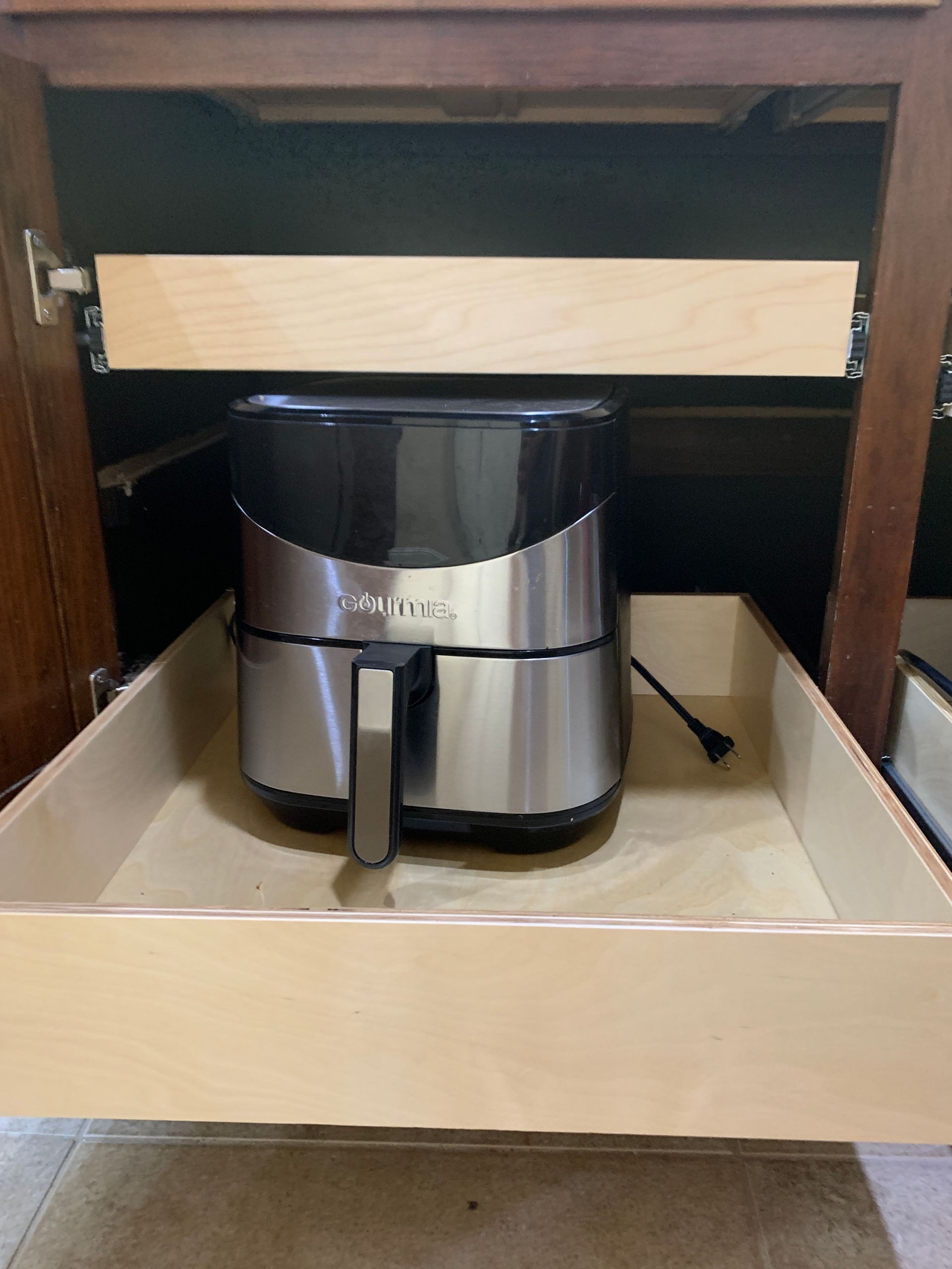 Air fryer on a pull-out drawer inside a brown cabinet. Drawer is open, cord plugged in.