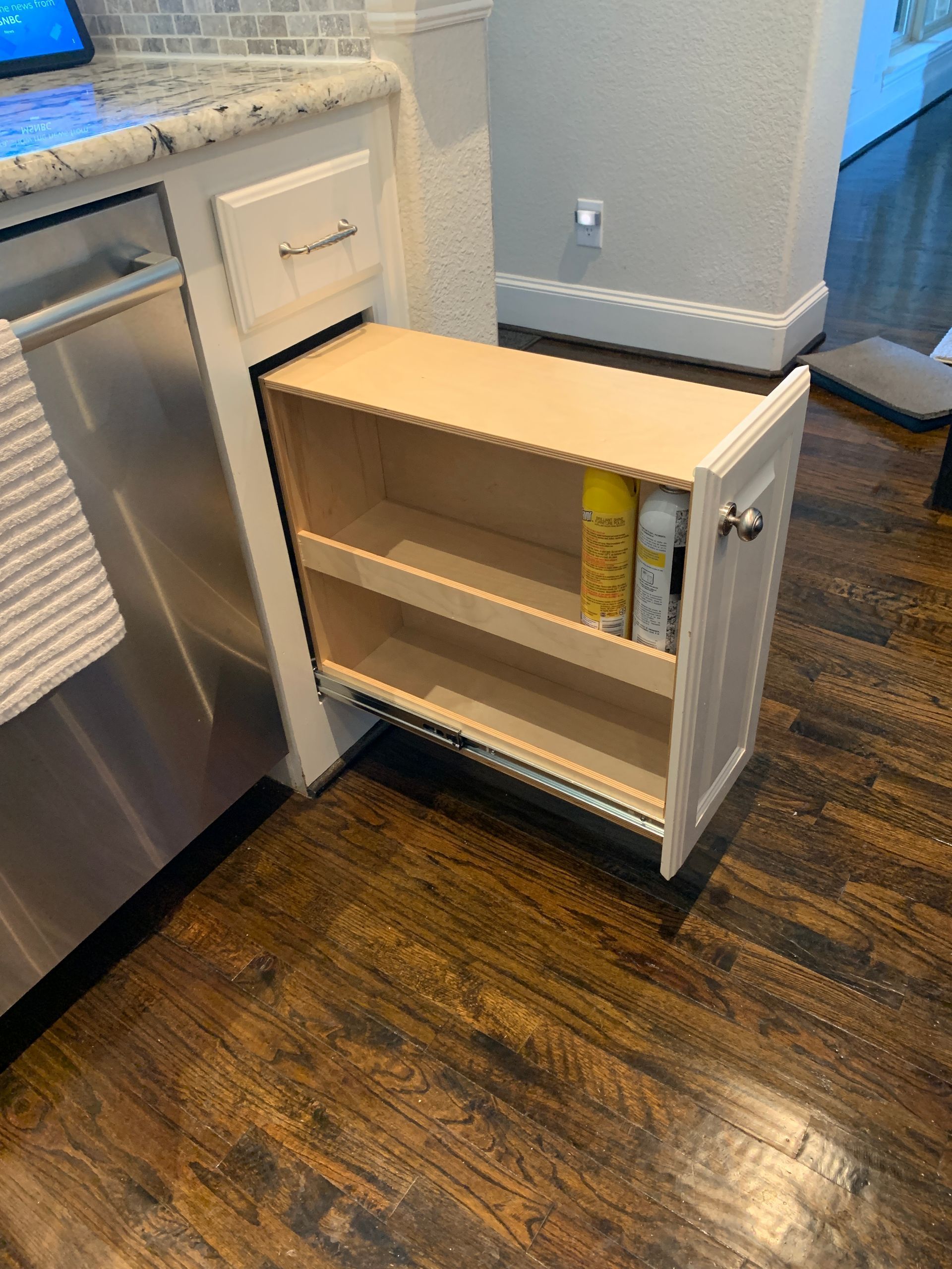 Pull-out cabinet with two shelves in a kitchen, holding cooking sprays, next to a stainless steel appliance and wood flooring.