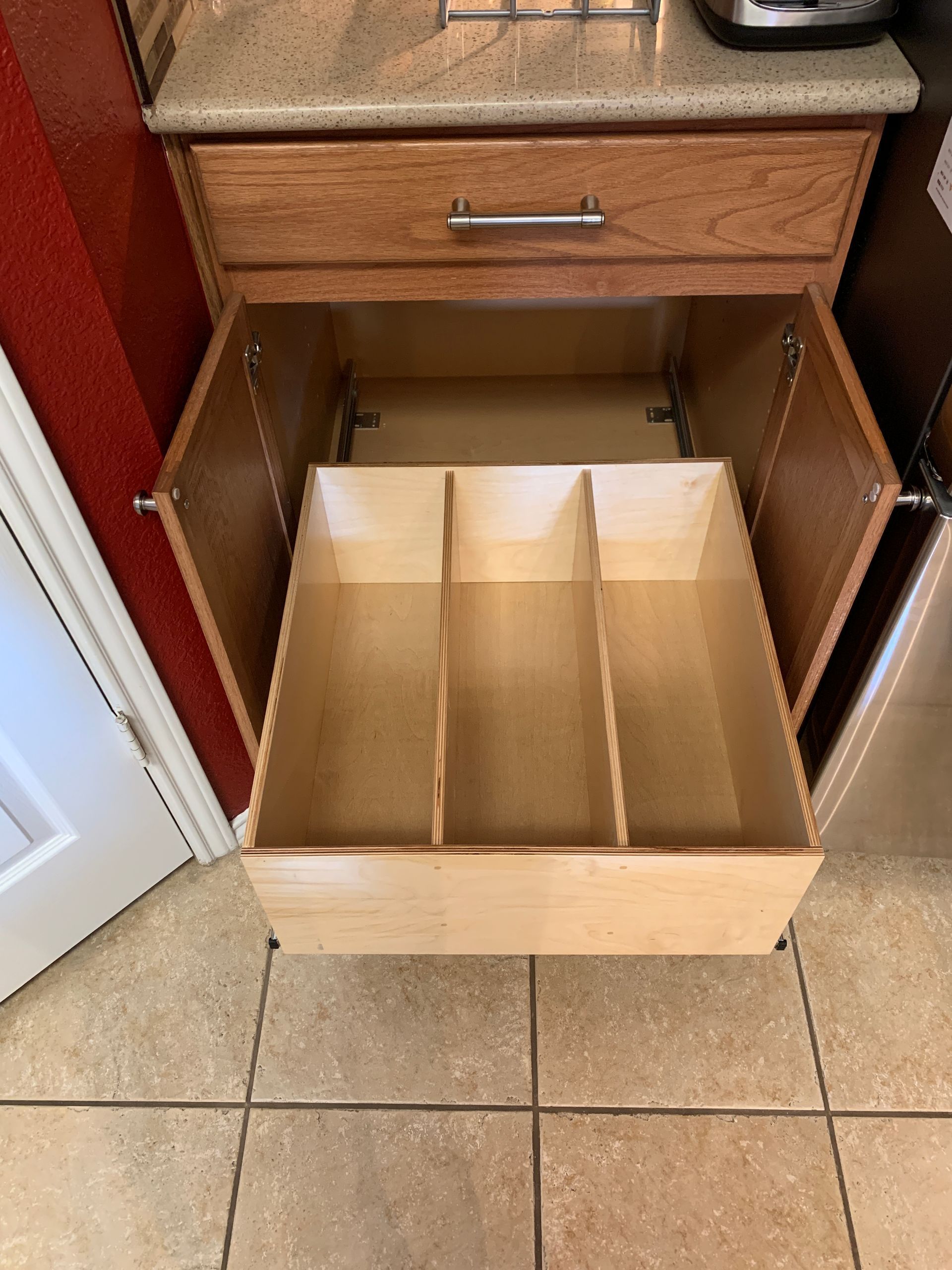 Wooden kitchen cabinet drawer open, showing three dividers for utensil storage.