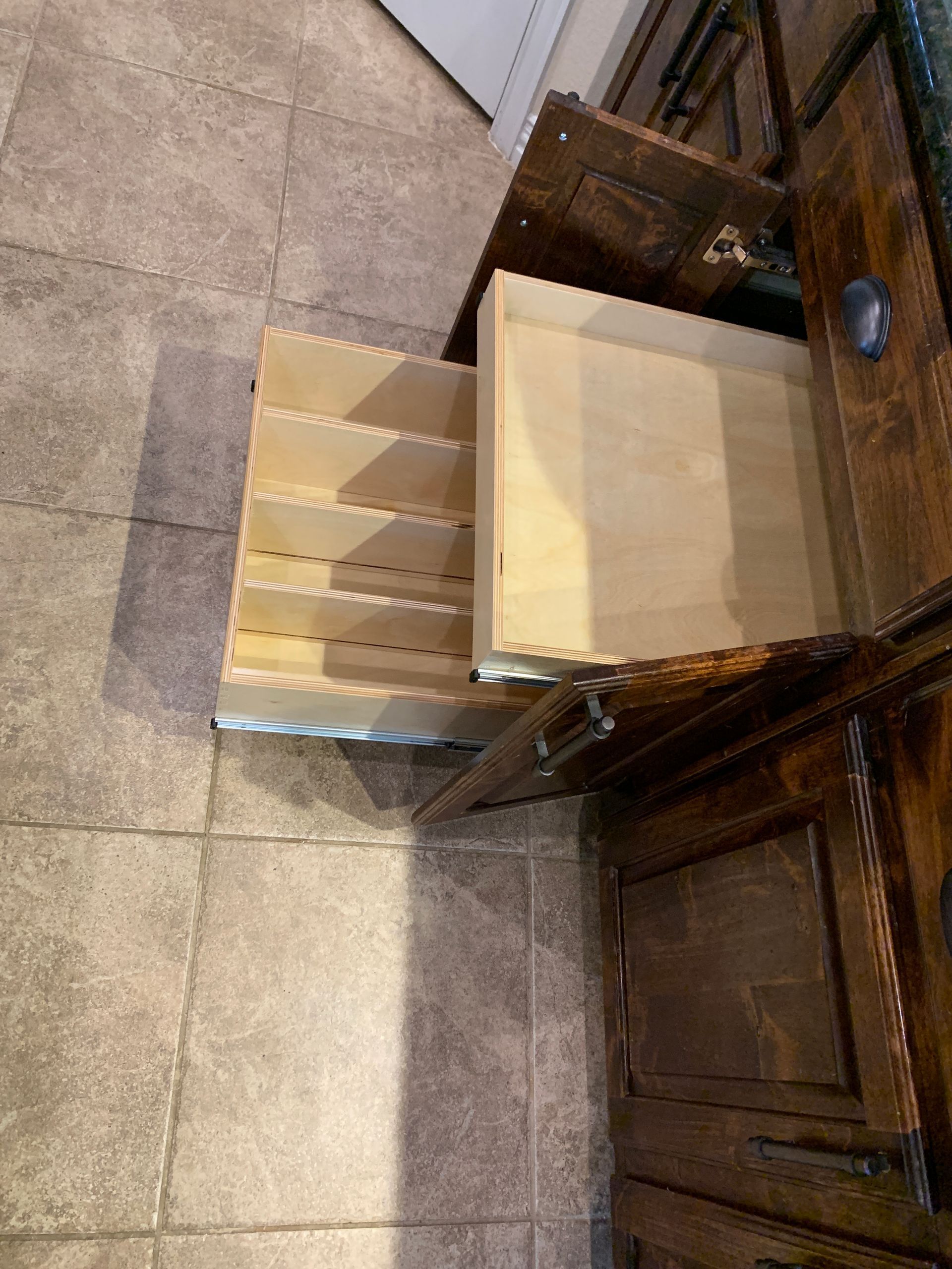 Opened wooden cabinet with pull-out drawers on a tiled floor.