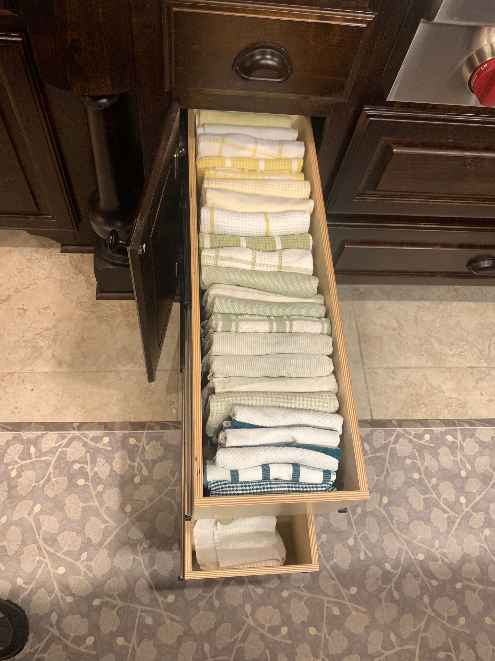 Open kitchen cabinet drawer filled with folded white and pastel dish towels.