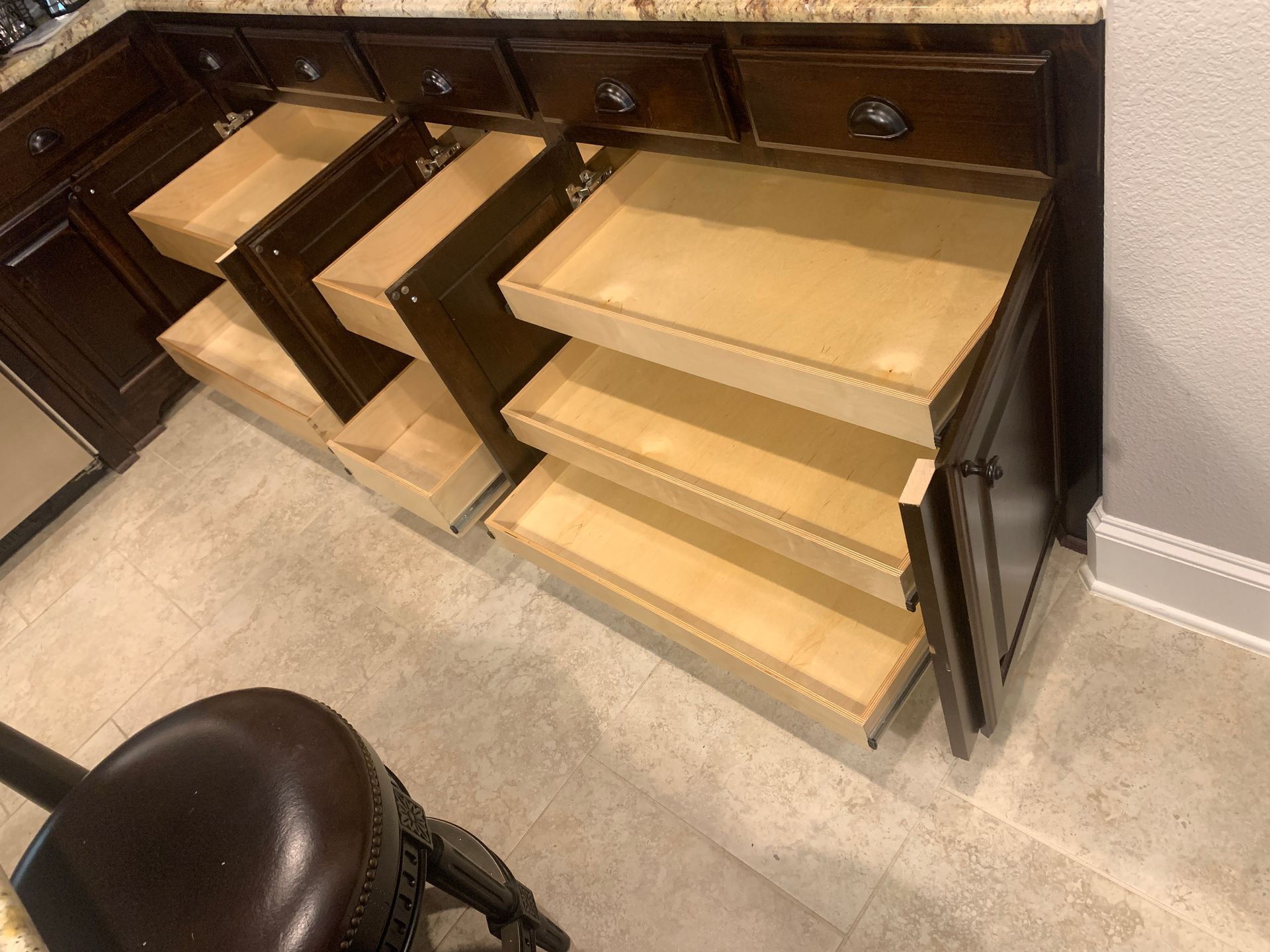 Kitchen cabinets with multiple pull-out drawers, partially open, against a beige wall and floor.