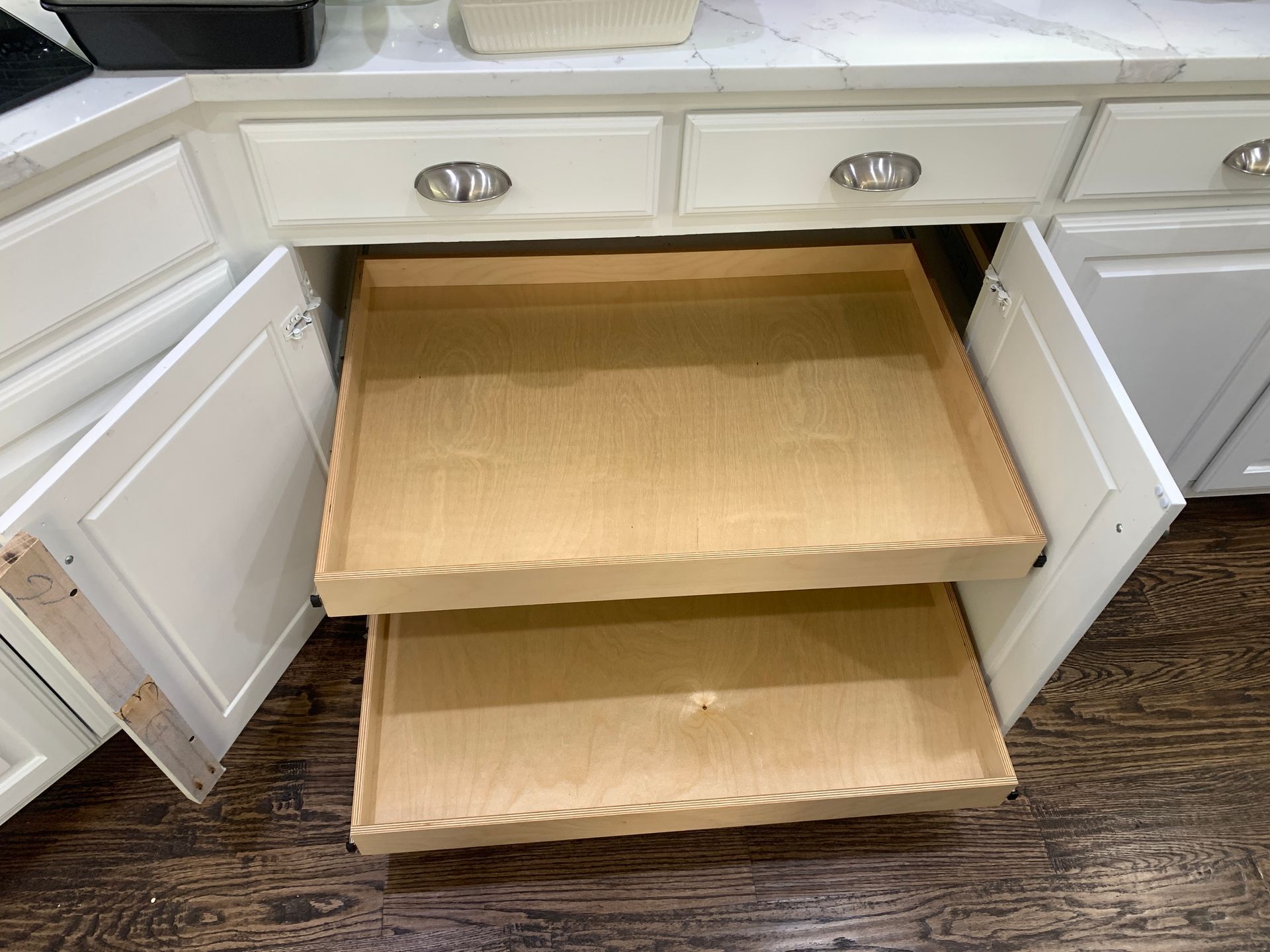 Open kitchen cabinet with pull-out wooden shelves, white doors, and a countertop.