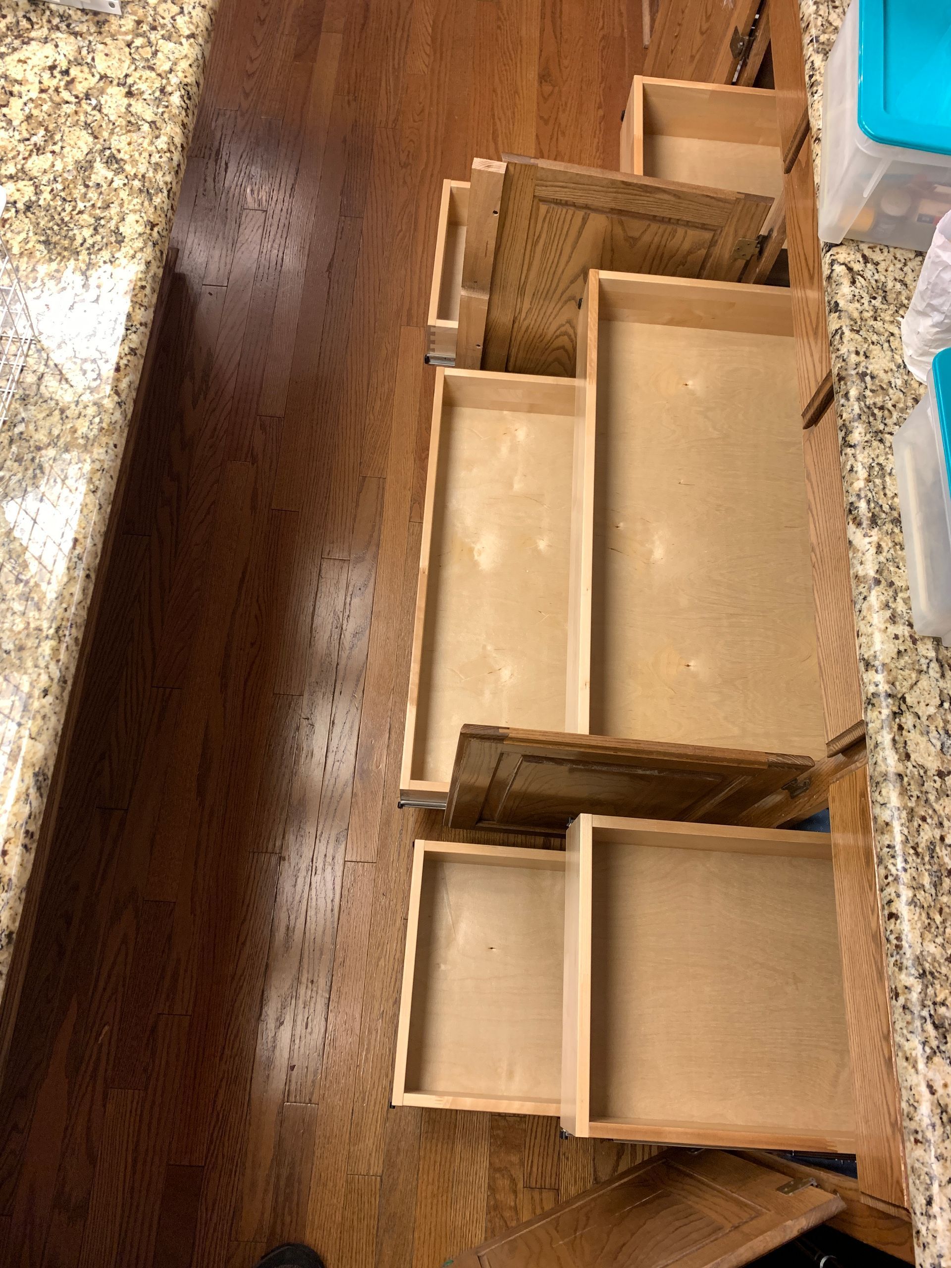 Open wooden kitchen drawers in a cabinet. The drawers are of varying sizes, on a wood floor, with a granite countertop.