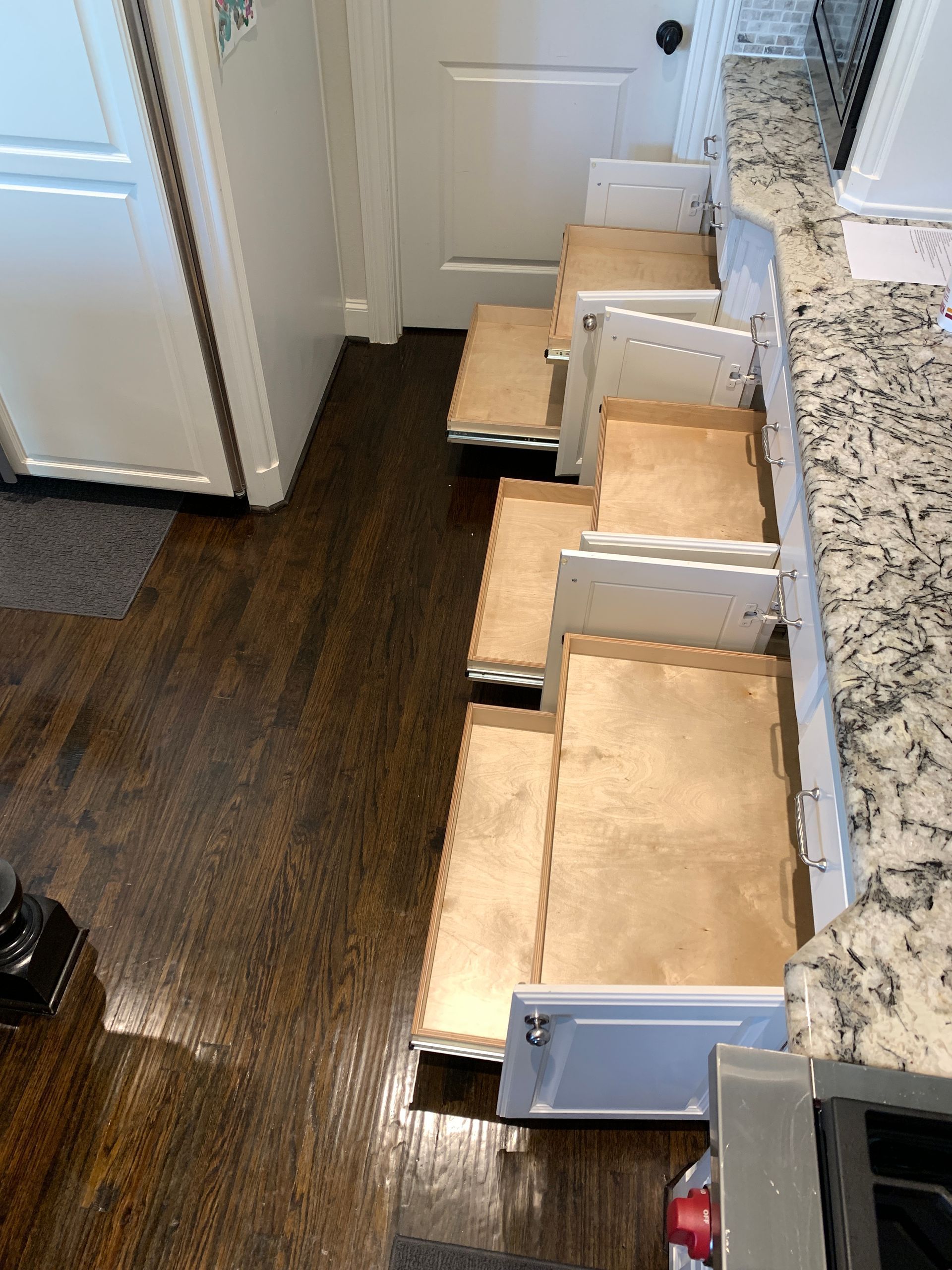 Open kitchen drawers of various sizes along a countertop. Drawers are wooden inside. Dark wood floor.