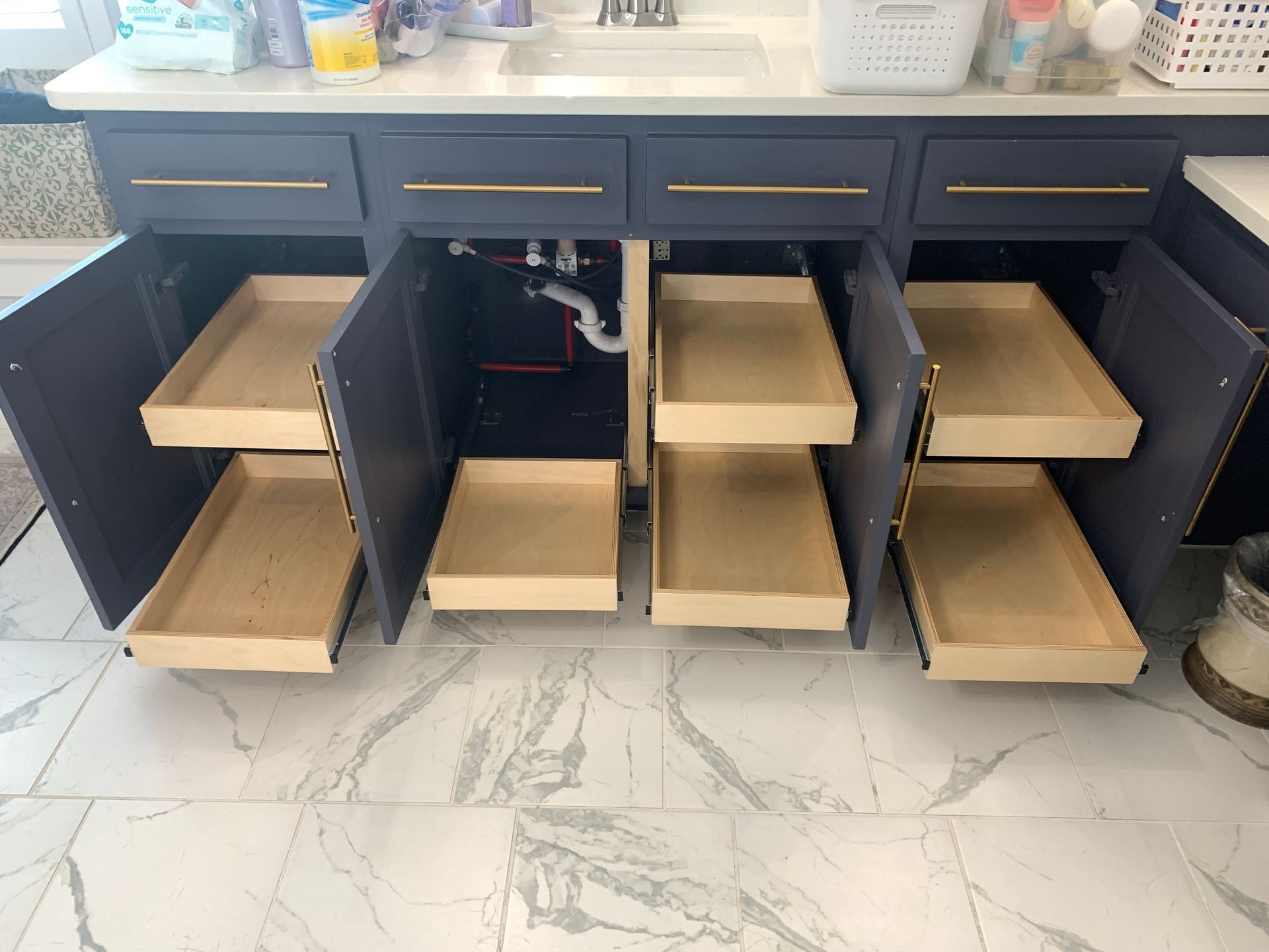 Navy blue bathroom vanity with pull-out drawers, gold hardware, and open doors showing the drawer interiors.