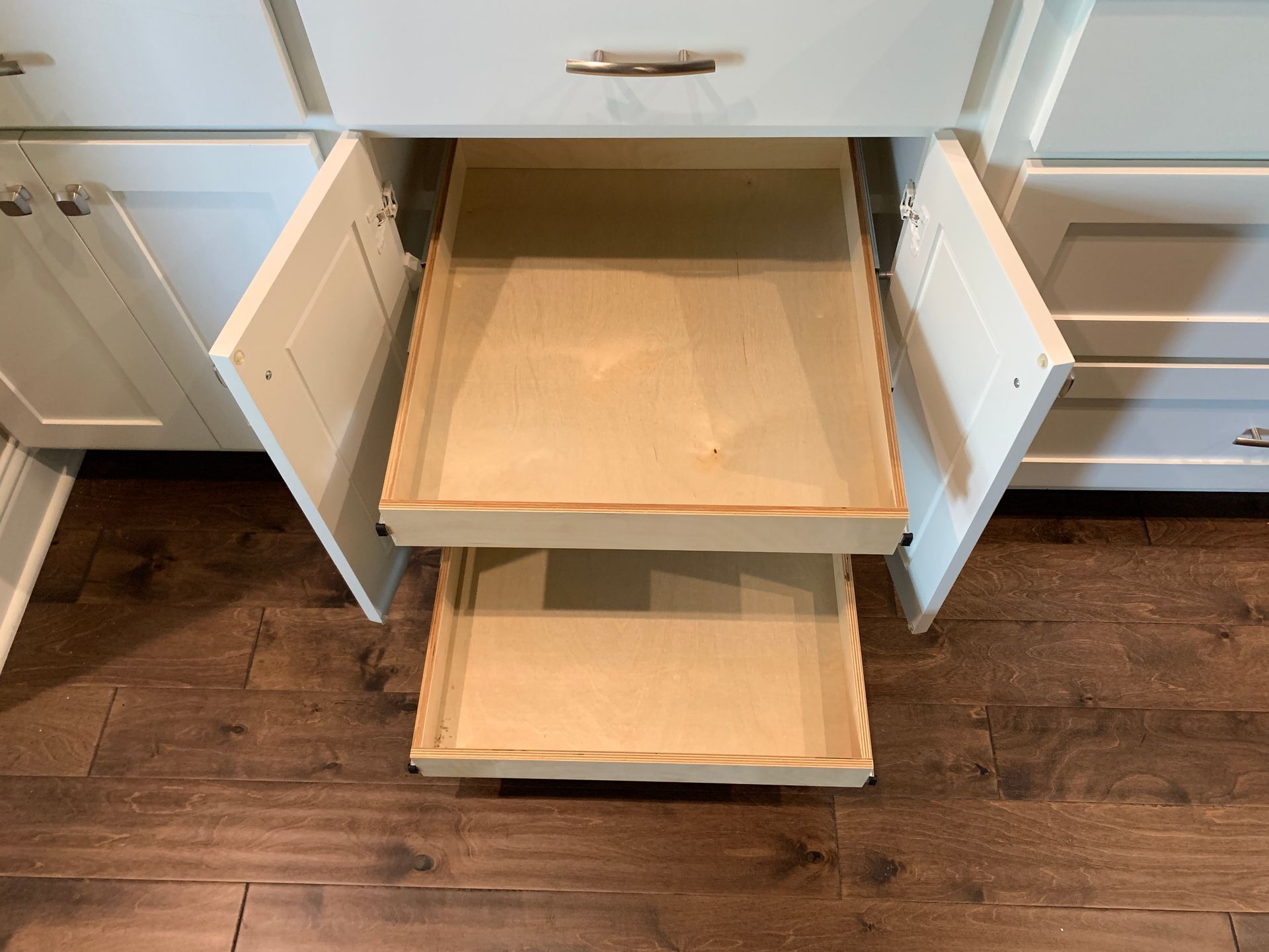 Cabinet with two open drawers, showing light-colored interiors. The cabinets are white, sitting on a wooden floor.