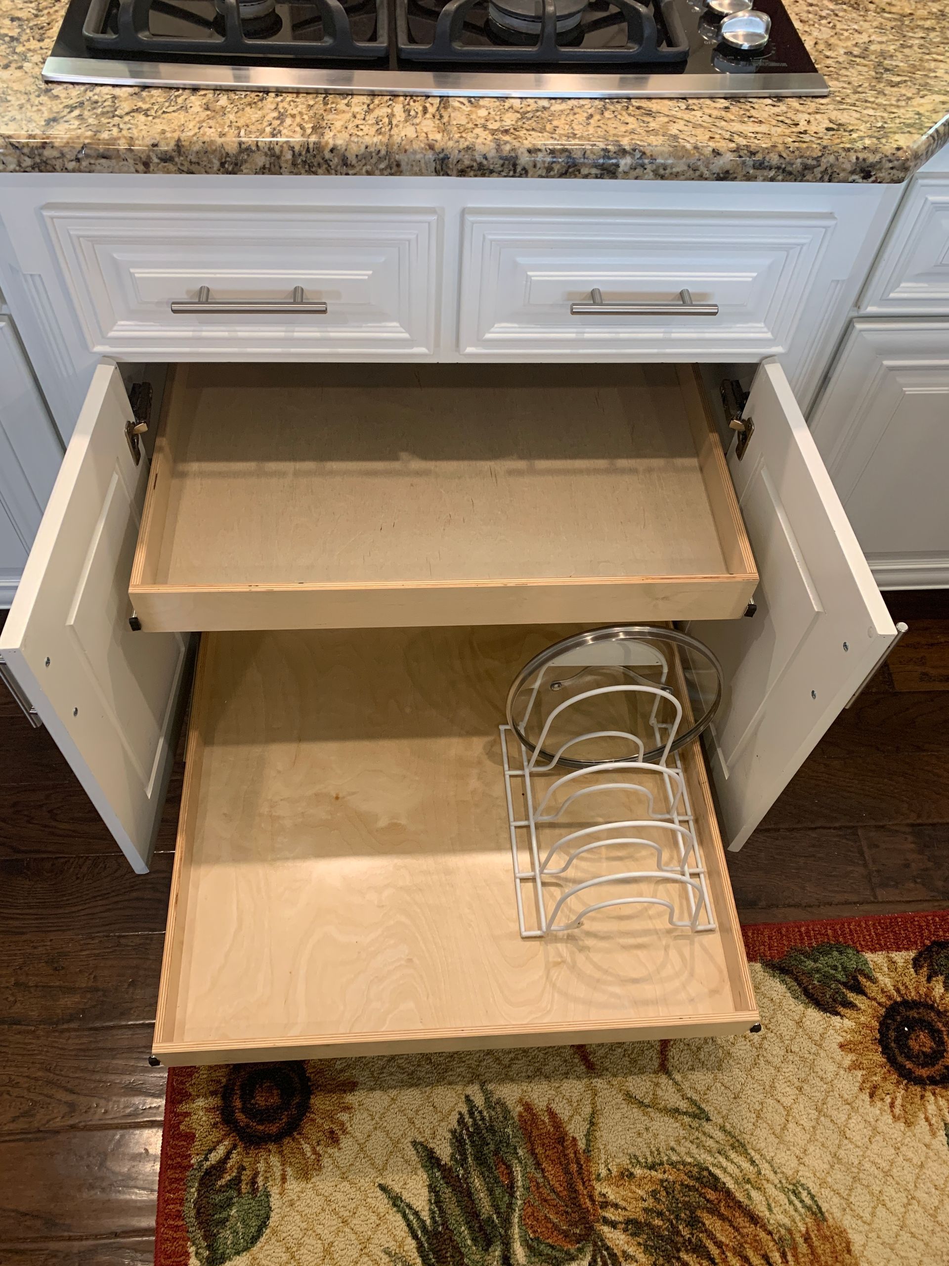 Open white kitchen cabinet with two pull-out shelves, one containing a pan organizer.