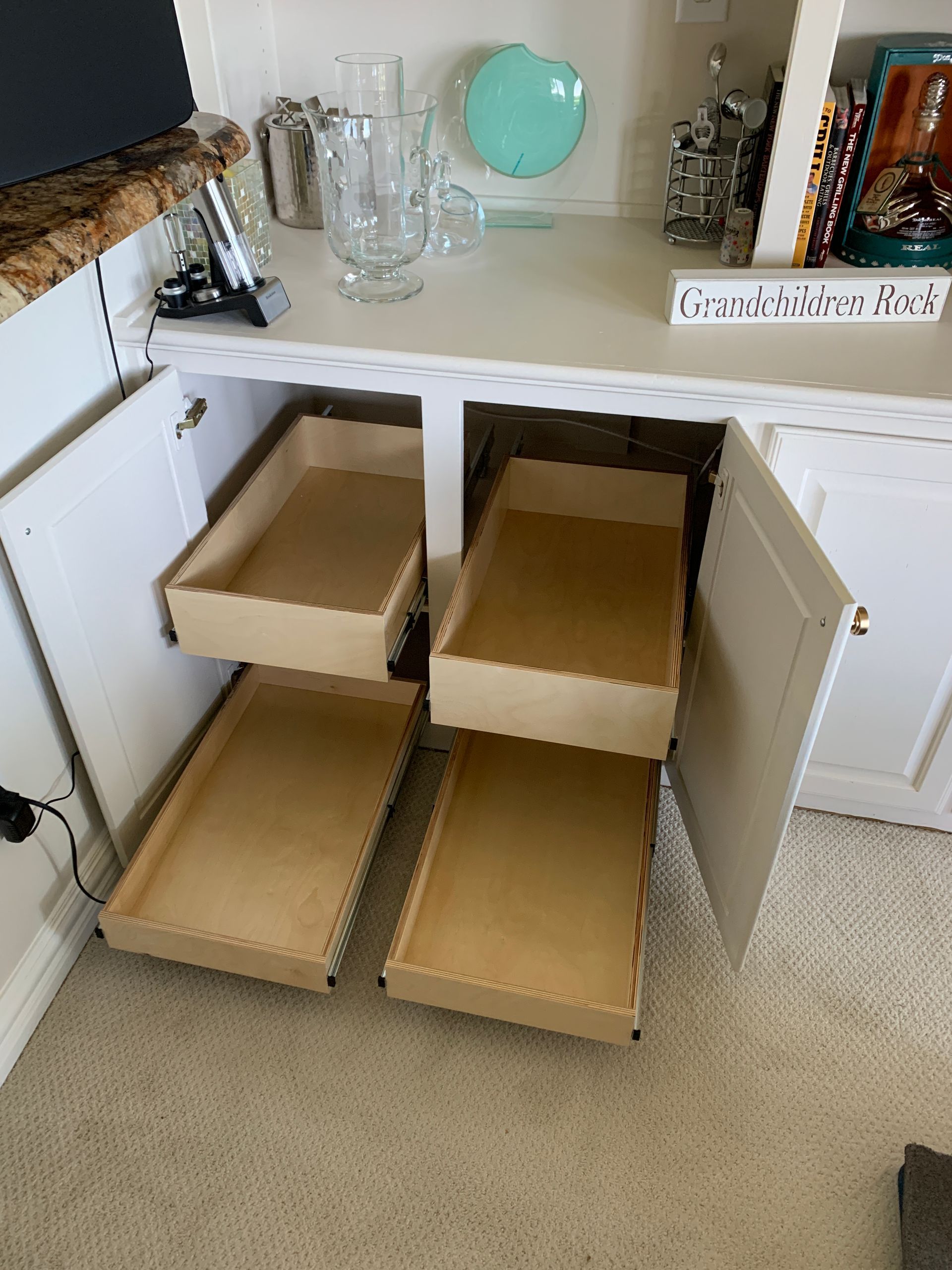 Open kitchen cabinet with four pull-out drawers, beige carpet, and white countertop.