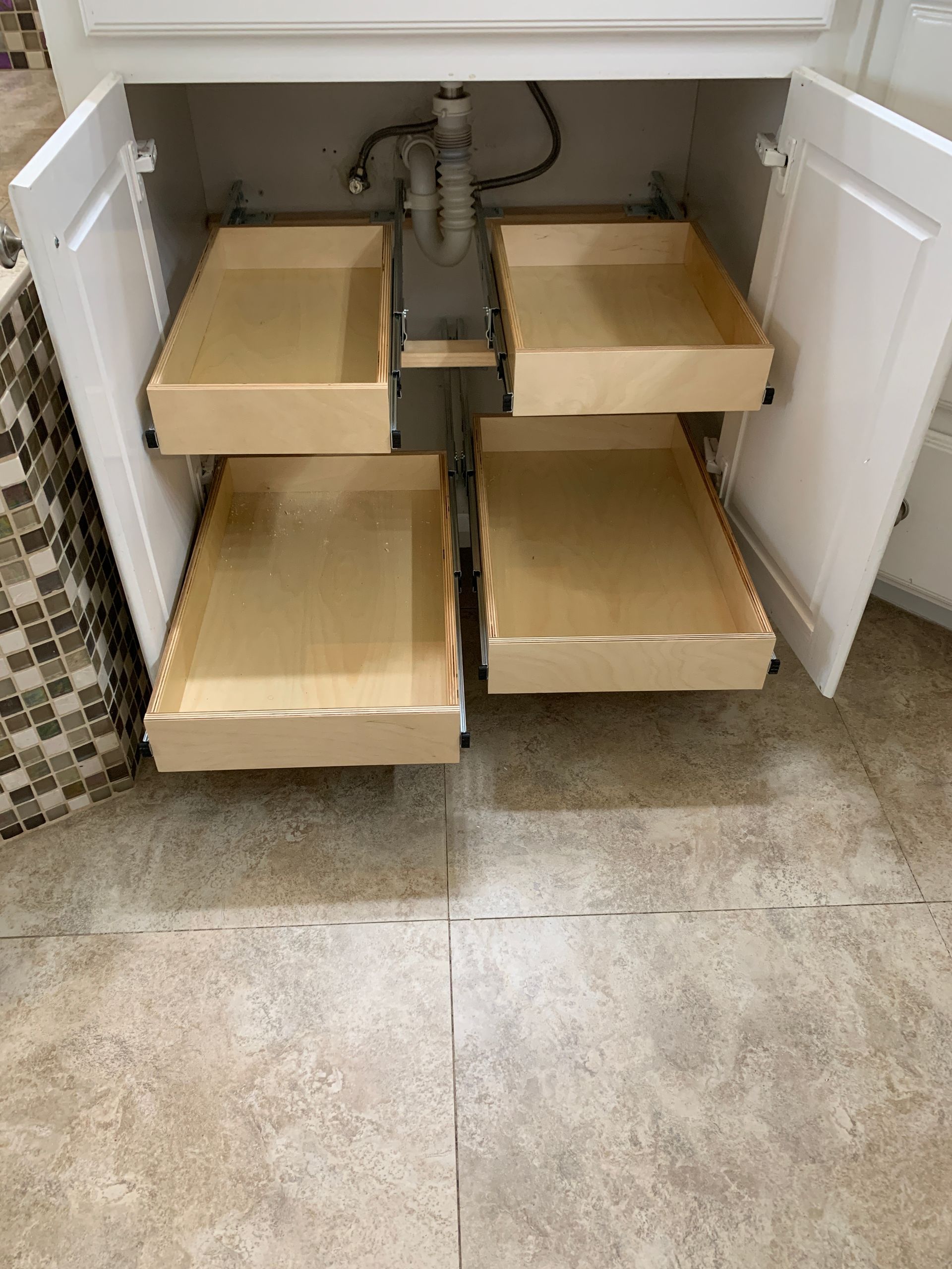 Bathroom vanity with four pull-out drawers, white cabinets, light wood drawers, and plumbing visible.