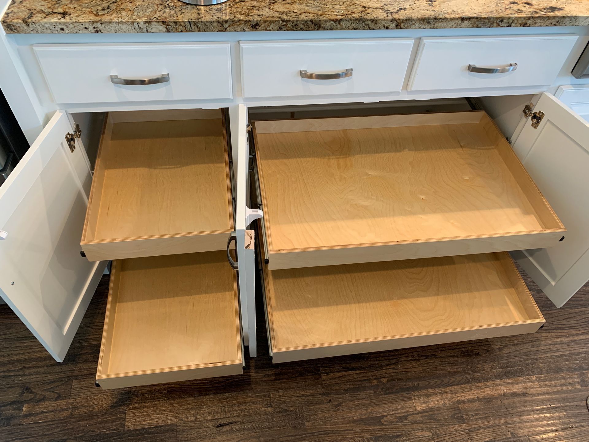 White kitchen cabinets with pull-out drawers, open to reveal empty shelves.
